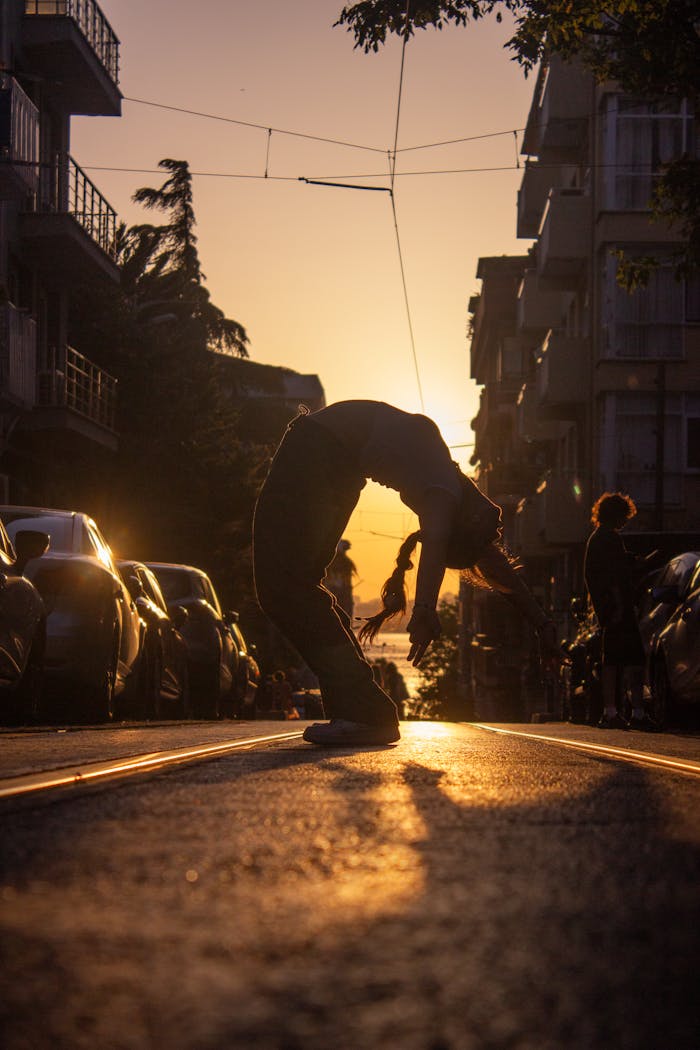 A dancer performing a dramatic silhouette pose on a city street during sunset, capturing the urban vibe.