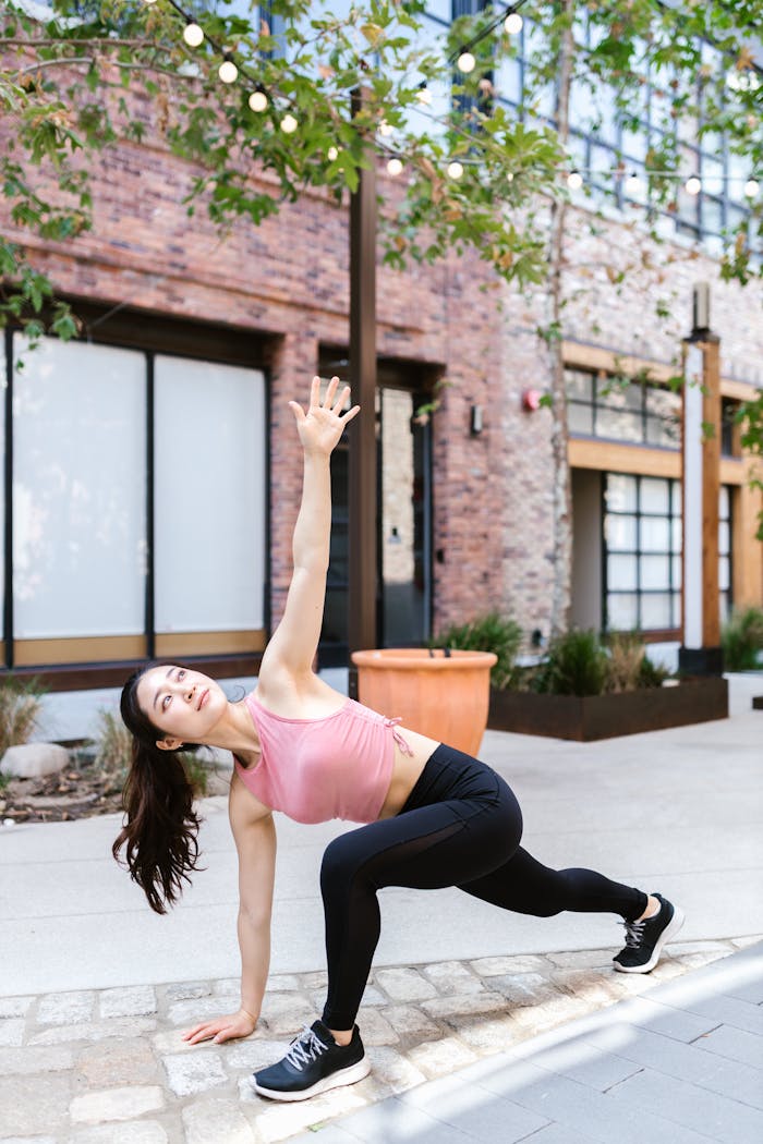Woman practicing outdoor fitness with a dynamic stretching pose in an urban setting.