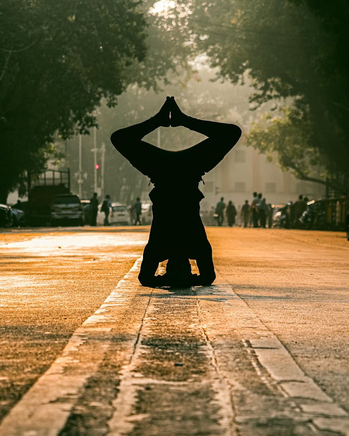 A person performs a headstand yoga pose on a sunlit Mumbai street, silhouetted at sunrise.