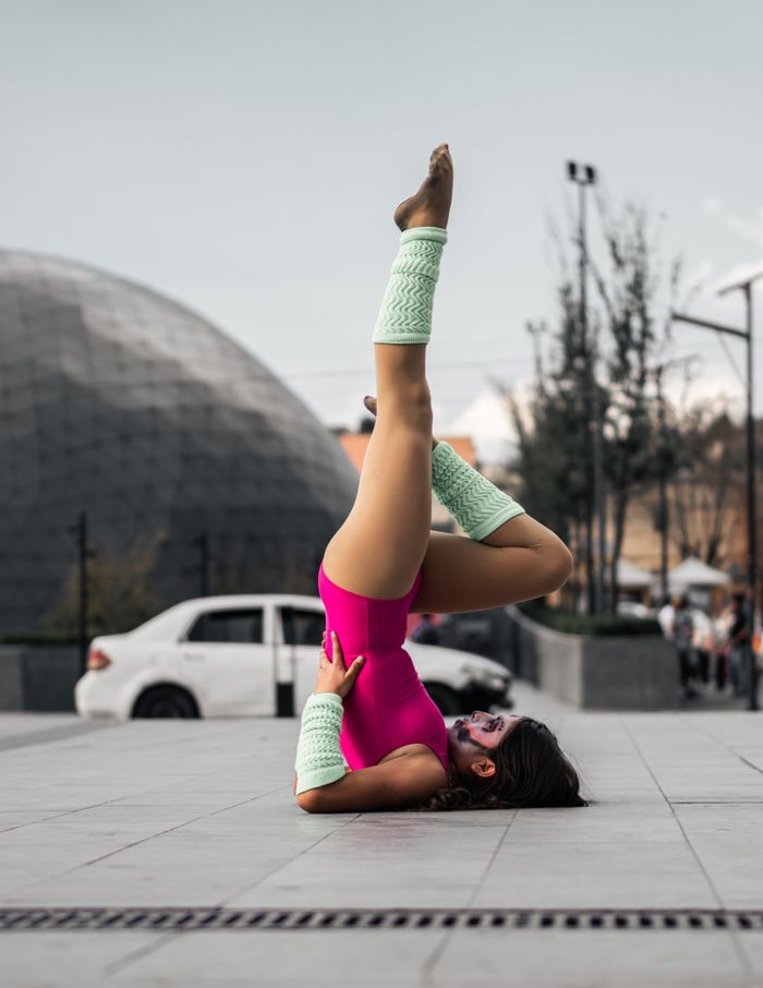 Woman in vibrant yoga pose on urban street wearing pink bodysuit.