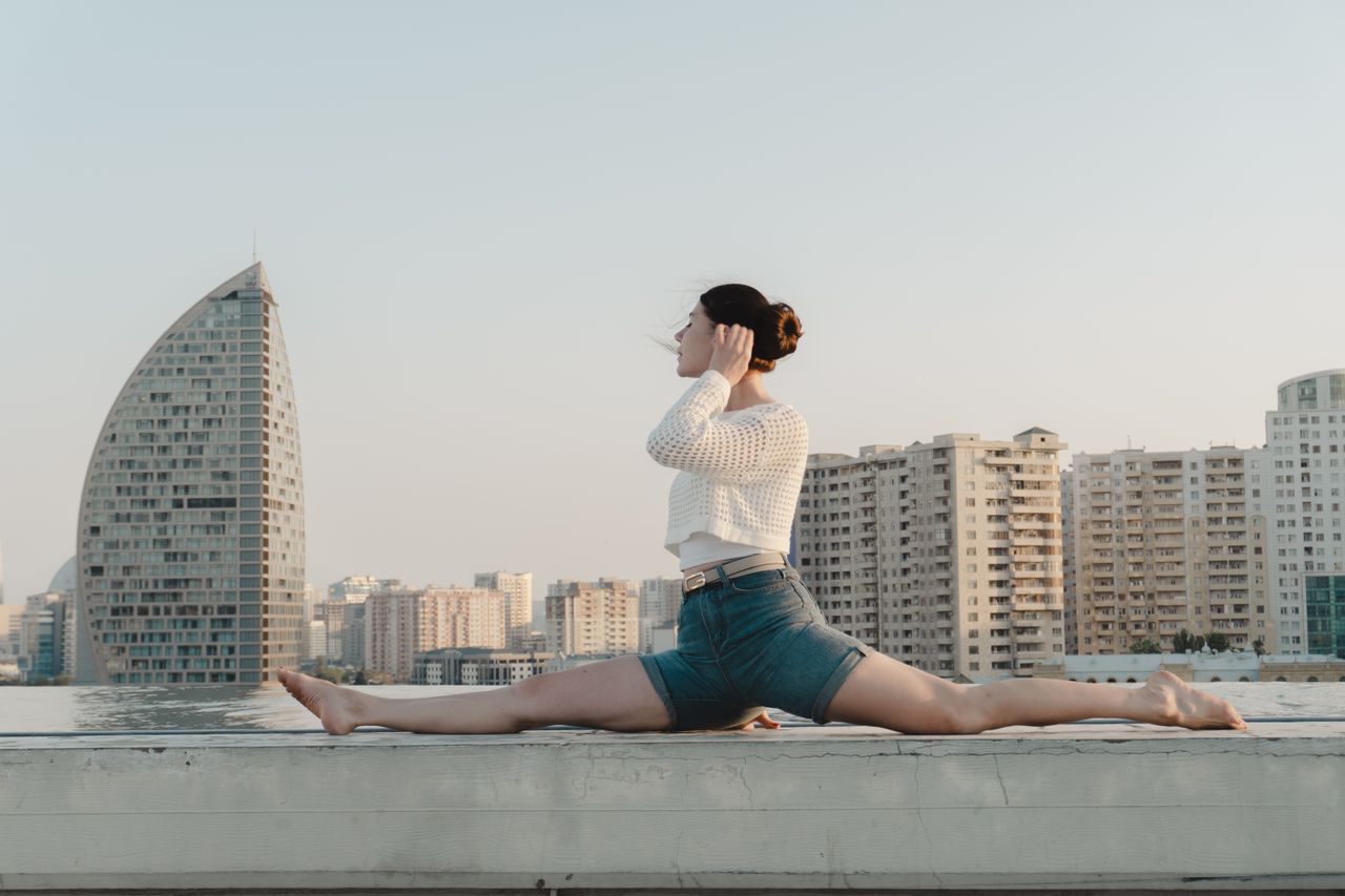 A woman is doing a split on a rooftop with a city skyline in the background.