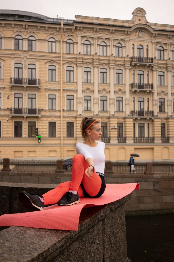A woman in activewear practices yoga on a mat in front of a historic building in a city.